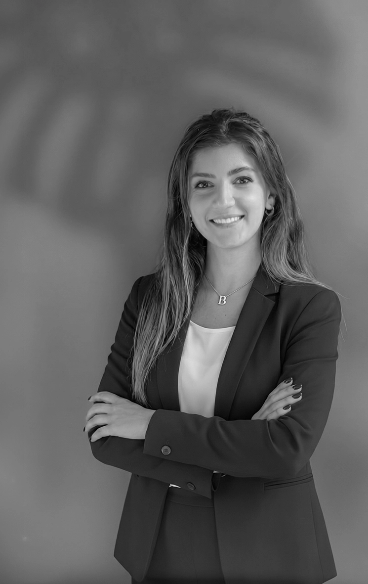 Beatrice Pirani in piedi davanti a una parete chiara, giacca scura e telefono in mano.